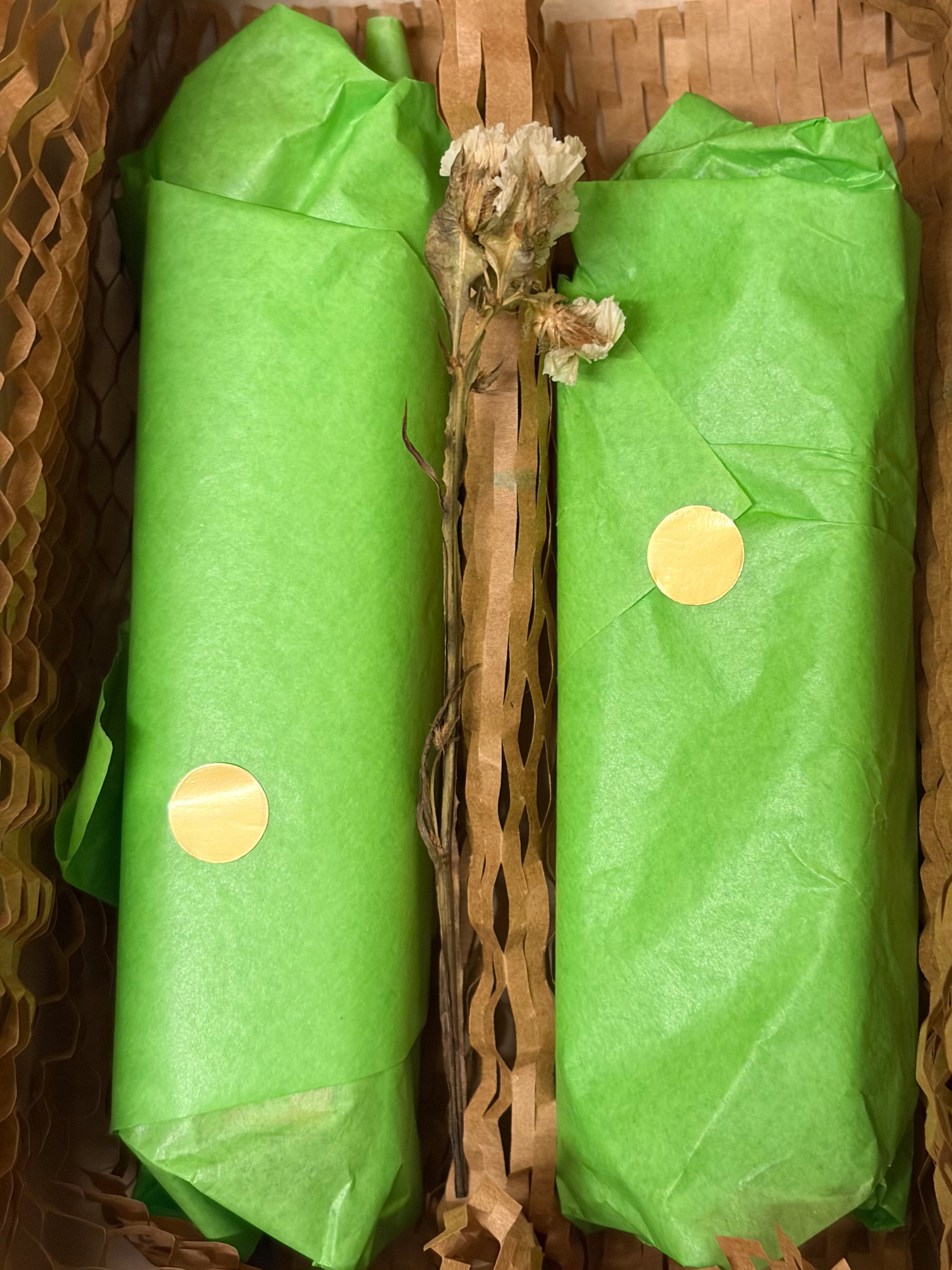 Two green tissue-paper wrapped packages with round gold stickers, placed side by side in a woven brown basket.
